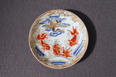 Een Chinese ijzerrode, grisaille, vergulde en overglazuur blauwe kop en schotel met karpers en een kraanvogel, Yongzheng